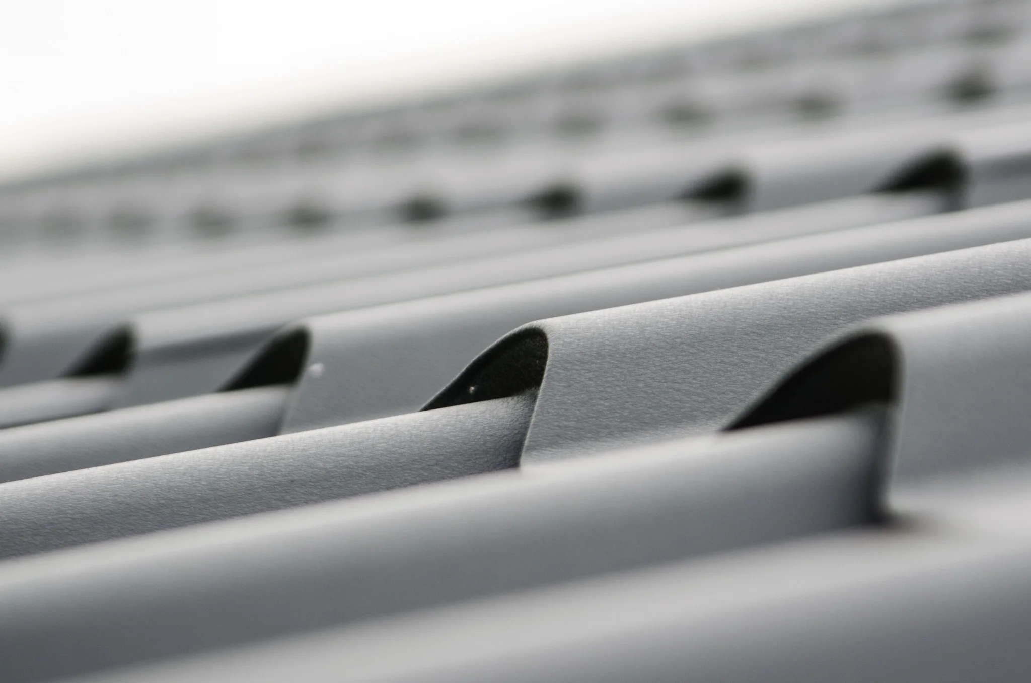 A close-up, shallow depth-of-field shot of grey metal roofing tiles displaying a smooth, repeating wave pattern.