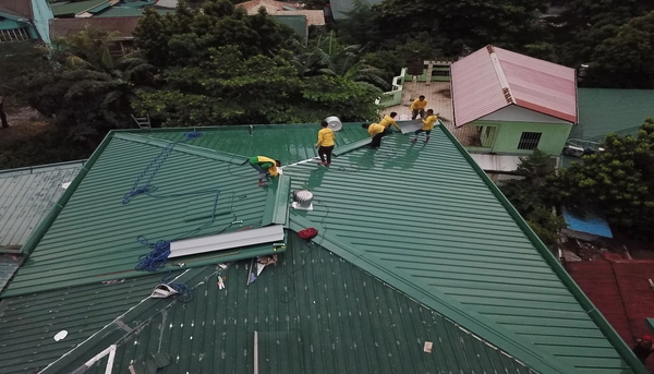An aerial view of a team of roofing contractors installing green metal roofing panels on a residential home.
